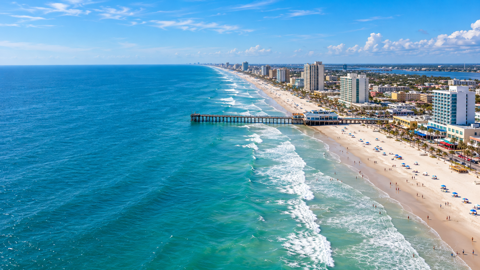 Sunlit Florida shoreline with ocean waves, a pier, and palm trees